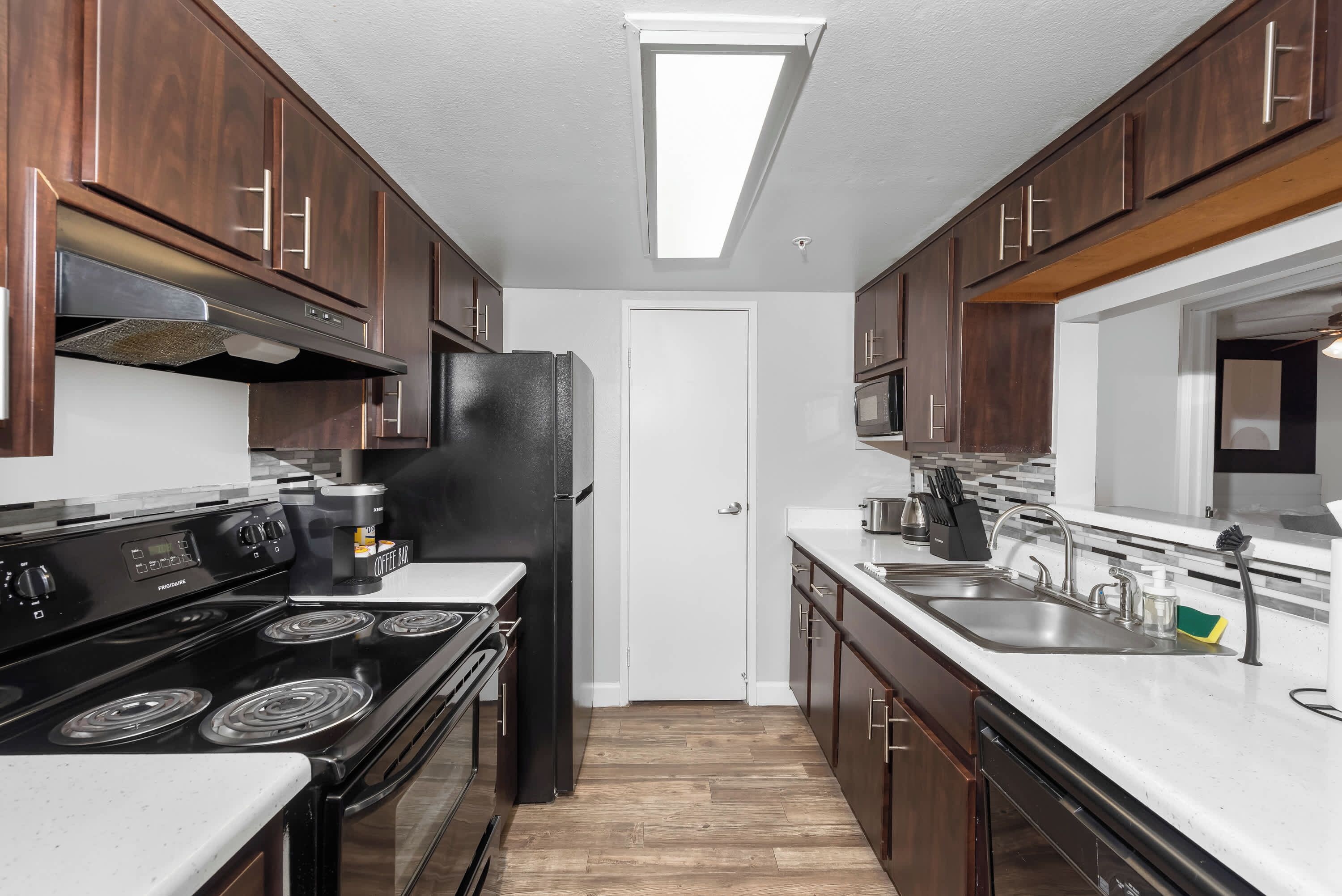 A compact kitchen with dark wooden cabinets, a black refrigerator, a stove, and a microwave.