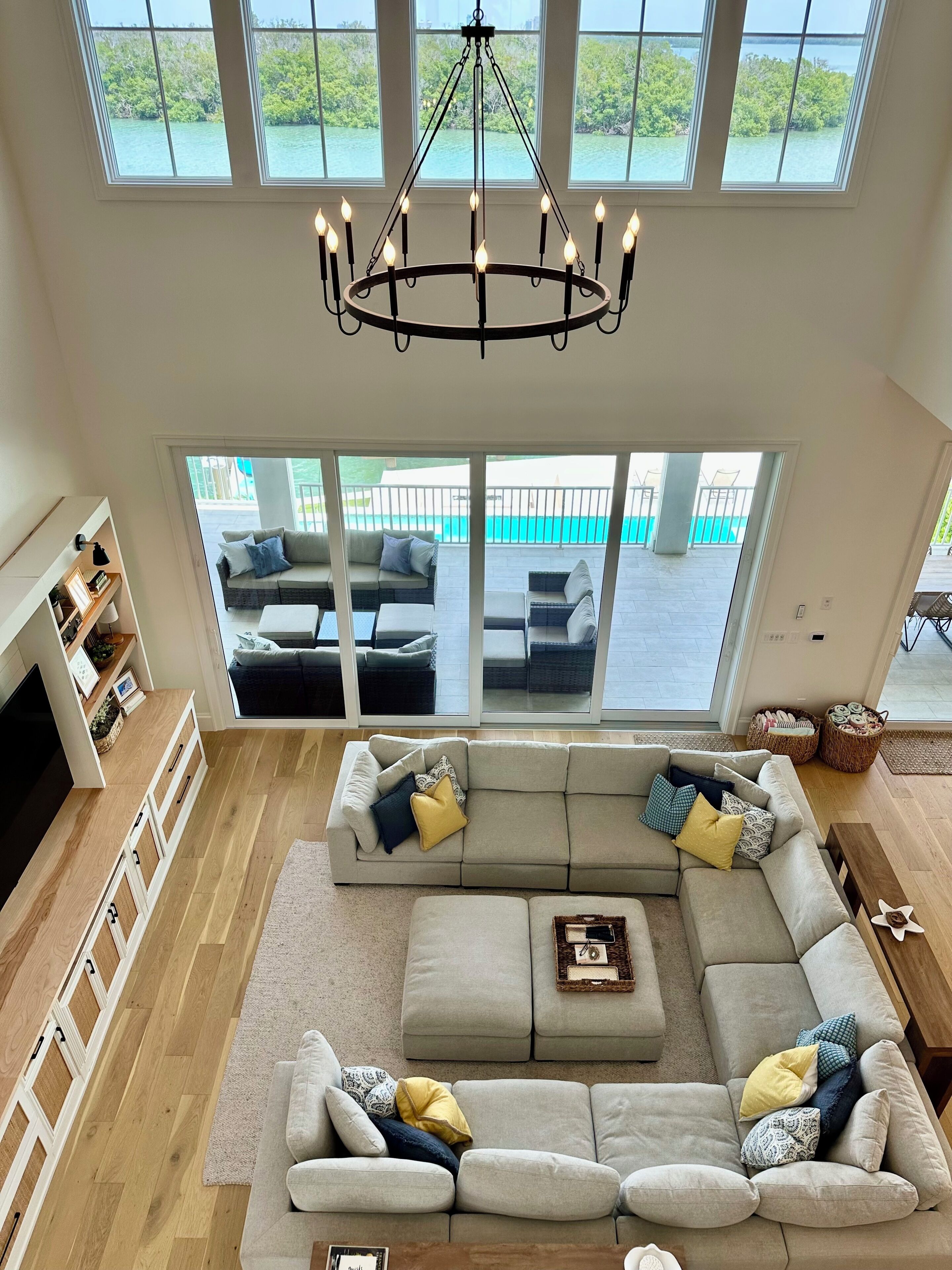 A spacious living room with a large sectional sofa, a chandelier, and a view of a balcony with outdoor furniture.