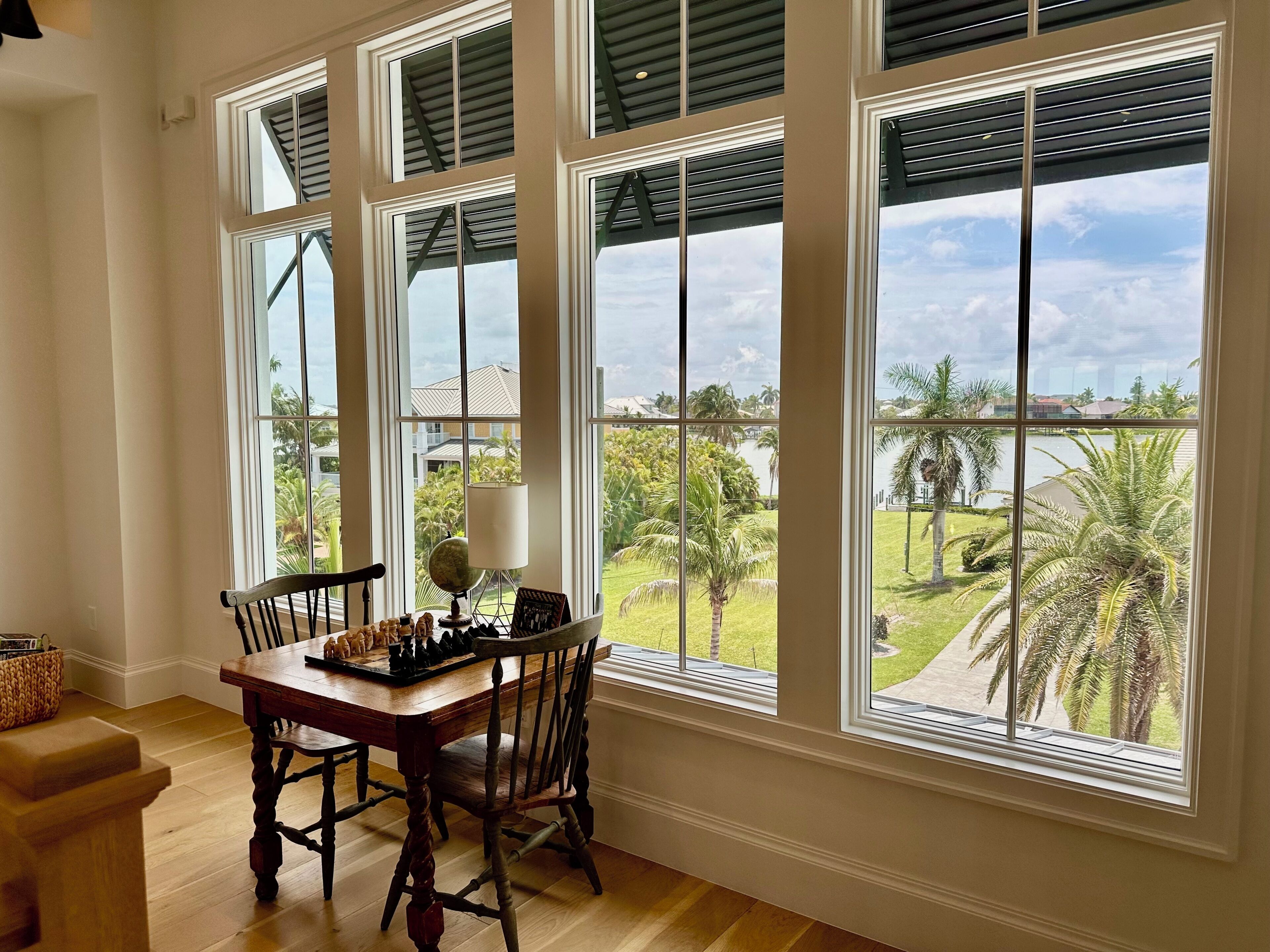 A dining area with a wooden table and chairs, large windows with shutters, and a view of a landscaped garden.