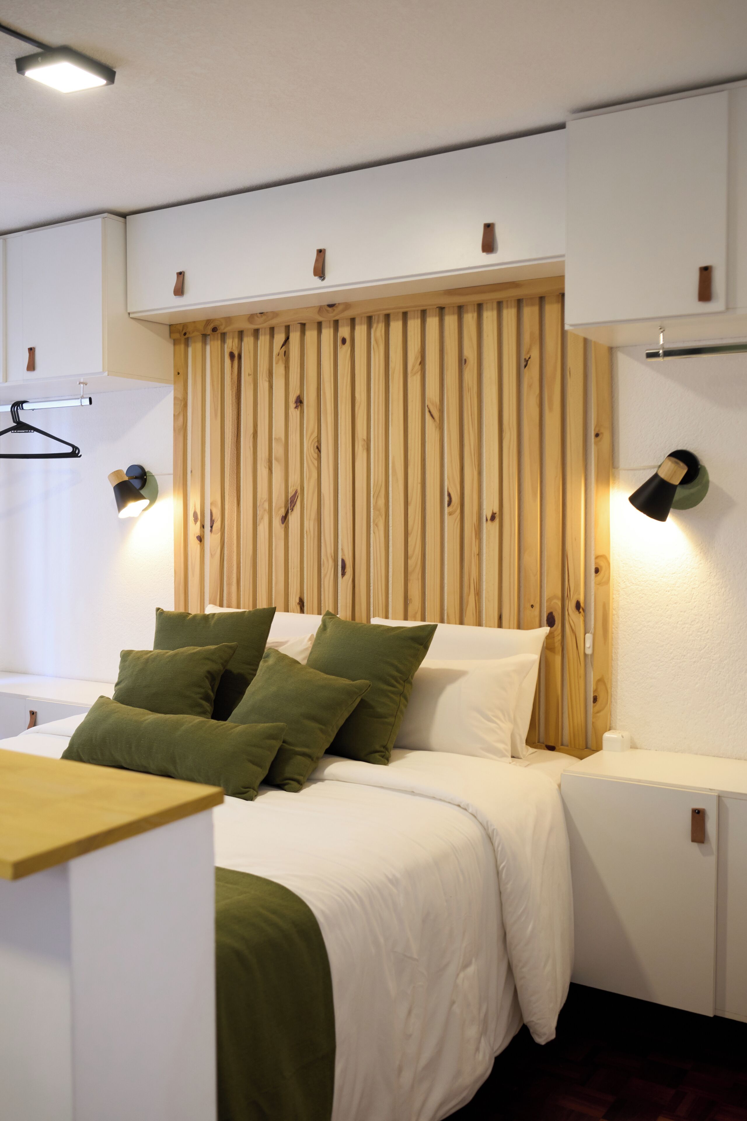 Ein modernes Schlafzimmer mit einem Holz-Kopfteil, einem Bett mit grün-weißer Bettwäsche und zwei Wandlampen.