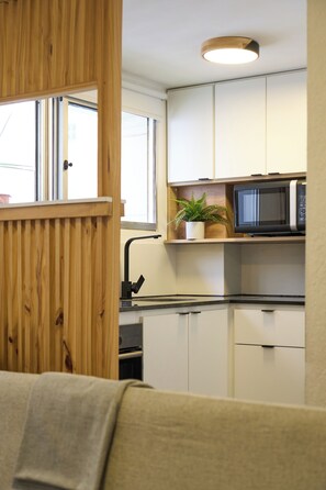 A compact kitchen with white cabinets, a microwave, and a potted plant on the countertop. - Modern studio apartment for 2 in Pocitos, just steps from the Rambla (Montevideo)