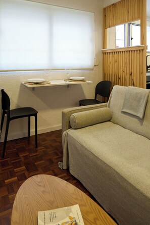 A cozy room with a sofa, a chair, a small table, and a window with blinds. - Modern studio apartment for 2 in Pocitos, just steps from the Rambla (Montevideo)