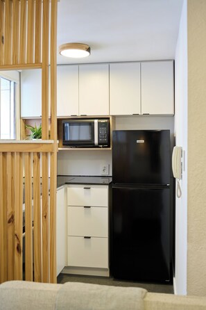 Eine kleine Küche mit einem schwarzen Kühlschrank, einer Mikrowelle und weißen Schränken.