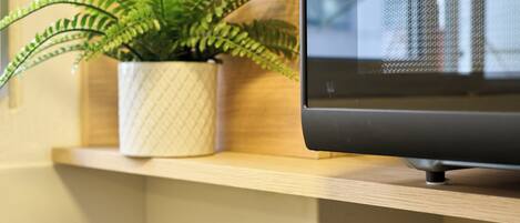 A flat-screen TV on a wooden shelf with a potted fern beside it.
