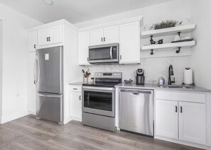 A modern kitchen with white cabinetry, stainless steel appliances, and a marble backsplash. - Slabtown TC Condo | Pets Welcome + Near Dog Park (Traverse City)