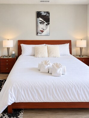 A hotel room with a large bed, two bedside tables with lamps, a wall-mounted painting, and a black and white rug. - Slabtown TC Condo | Pets Welcome + Near Dog Park (Traverse City)