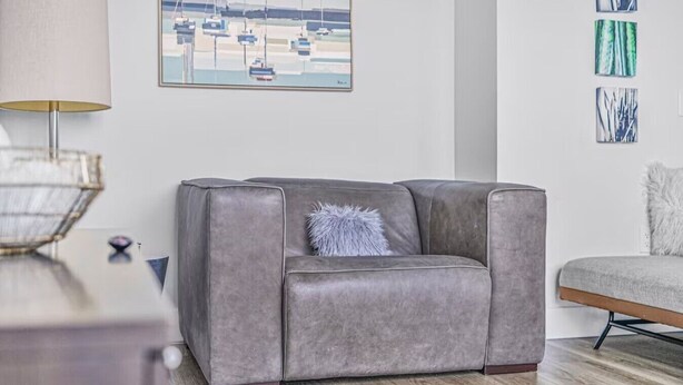 Ein graues Ledersofa mit einem flauschigen Kissen, ein gerahmtes Bild von Booten und abstrakte Kunst an der Wand.