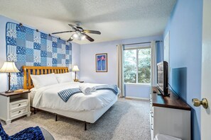 A neatly arranged bedroom with a bed, bedside lamps, a ceiling fan, a television, and a window with curtains. - The Broadmoor Condo | 2 Queens + Garage (Colorado Springs)