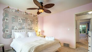 Ein Schlafzimmer mit einem großen Bett, einem Deckenventilator, einer Wandteppich und einem Nachttisch mit Lampe.