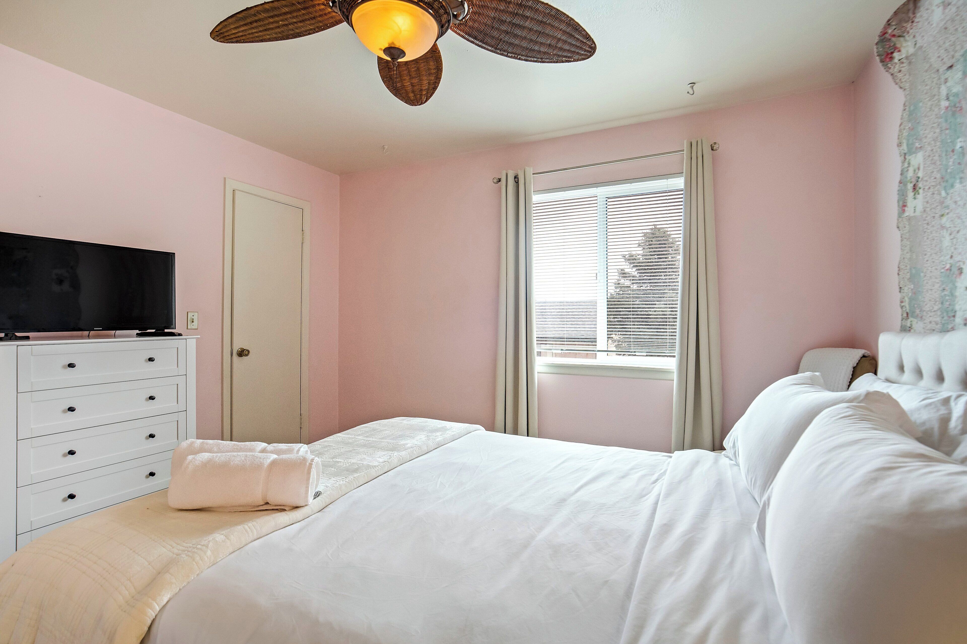 A bedroom with a bed, a dresser, a television, a ceiling fan, and a window with blinds.