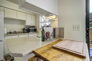 A kitchen with white cabinets, a microwave, a coffee maker, and a bottle of olive oil on the counter. - The Broadmoor Condo | 2 Queens + Garage (Colorado Springs)