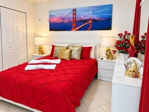 A hotel room with a red bedspread, a painting of a bridge, and a statue of a lion on the nightstand.