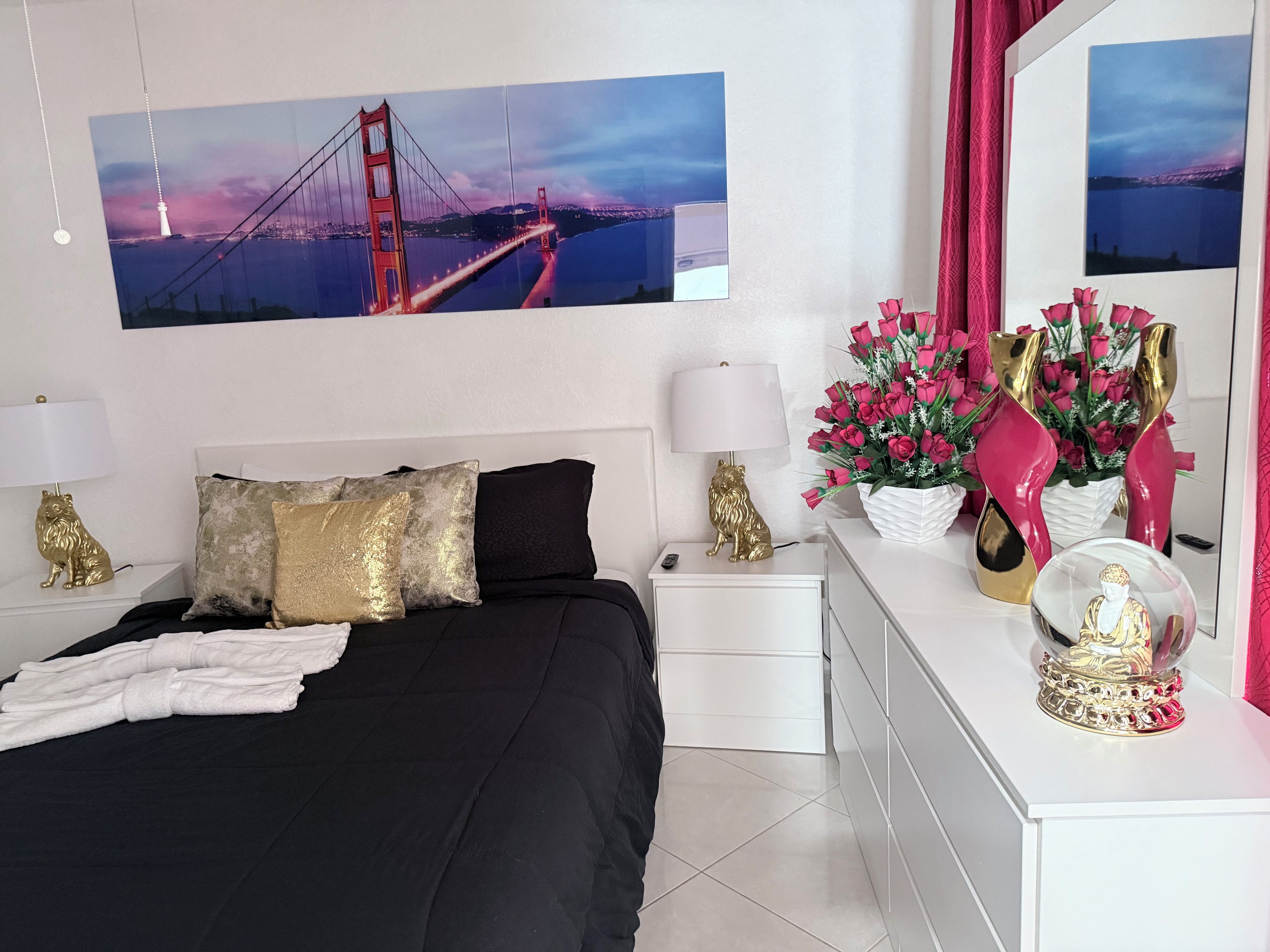 A hotel room with a bed, nightstands, a dresser, a mirror, and a large picture of the Golden Gate Bridge.