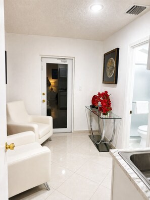 A modern living room with a white sofa, a glass coffee table, and a red flower arrangement. - Private Miami Suite (Miami)