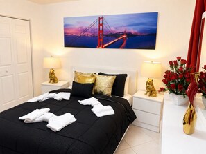 A hotel room with a bed, two bedside tables, a nightstand, a painting of a bridge, and a vase with red flowers. - Private Miami Suite (Miami)