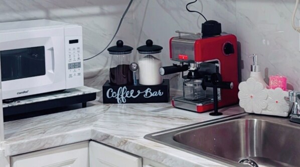 A kitchen with a white microwave, a coffee machine, a coffee bar, and a sink.