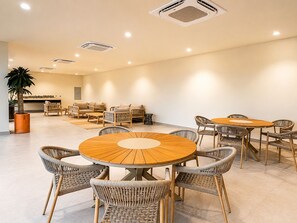 A spacious indoor area with multiple round wooden tables and wicker chairs, surrounded by sofas and a potted plant. - CASA CIAN • LUXURY PENTHOUSE SUITE • OCEAN & ARCH VIEWS • PRIVATE ROOFTOP (Cabo San Lucas)