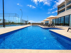 A swimming pool with lounge chairs and umbrellas, surrounded by a fence and modern buildings. - CASA CIAN • LUXURY PENTHOUSE SUITE • OCEAN & ARCH VIEWS • PRIVATE ROOFTOP (Cabo San Lucas)
