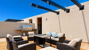 Eine Terrasse im Freien mit Korbmöbeln, einem Grill und Lichterketten.