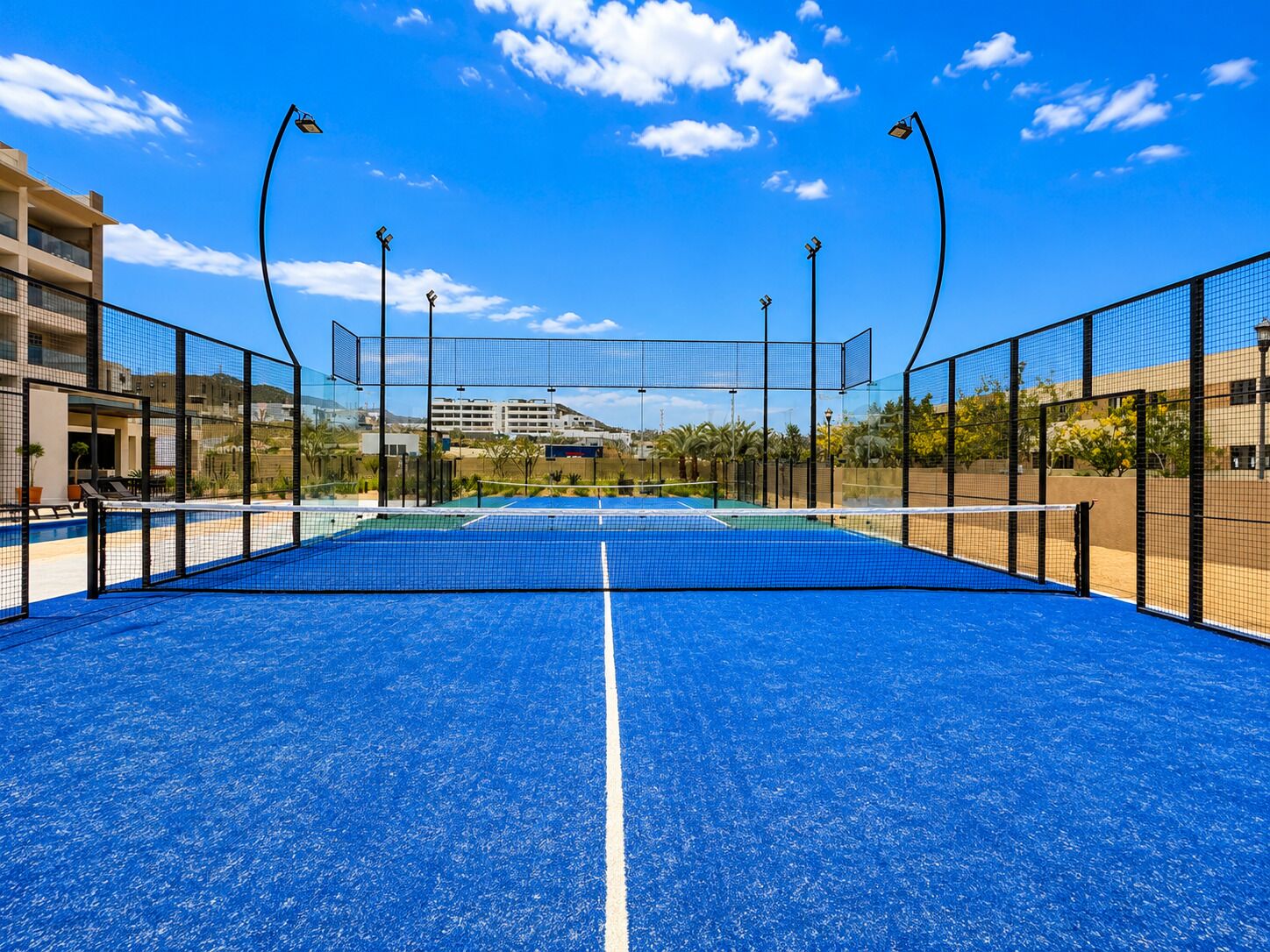 Cancha de tennis a l'aire lliure amb xarxa, envoltada per una tanca i una zona de piscina al fons.