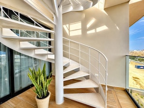 Ein modernes Interieur mit einer Wendeltreppe, großen Fenstern und einer Topfpflanze.