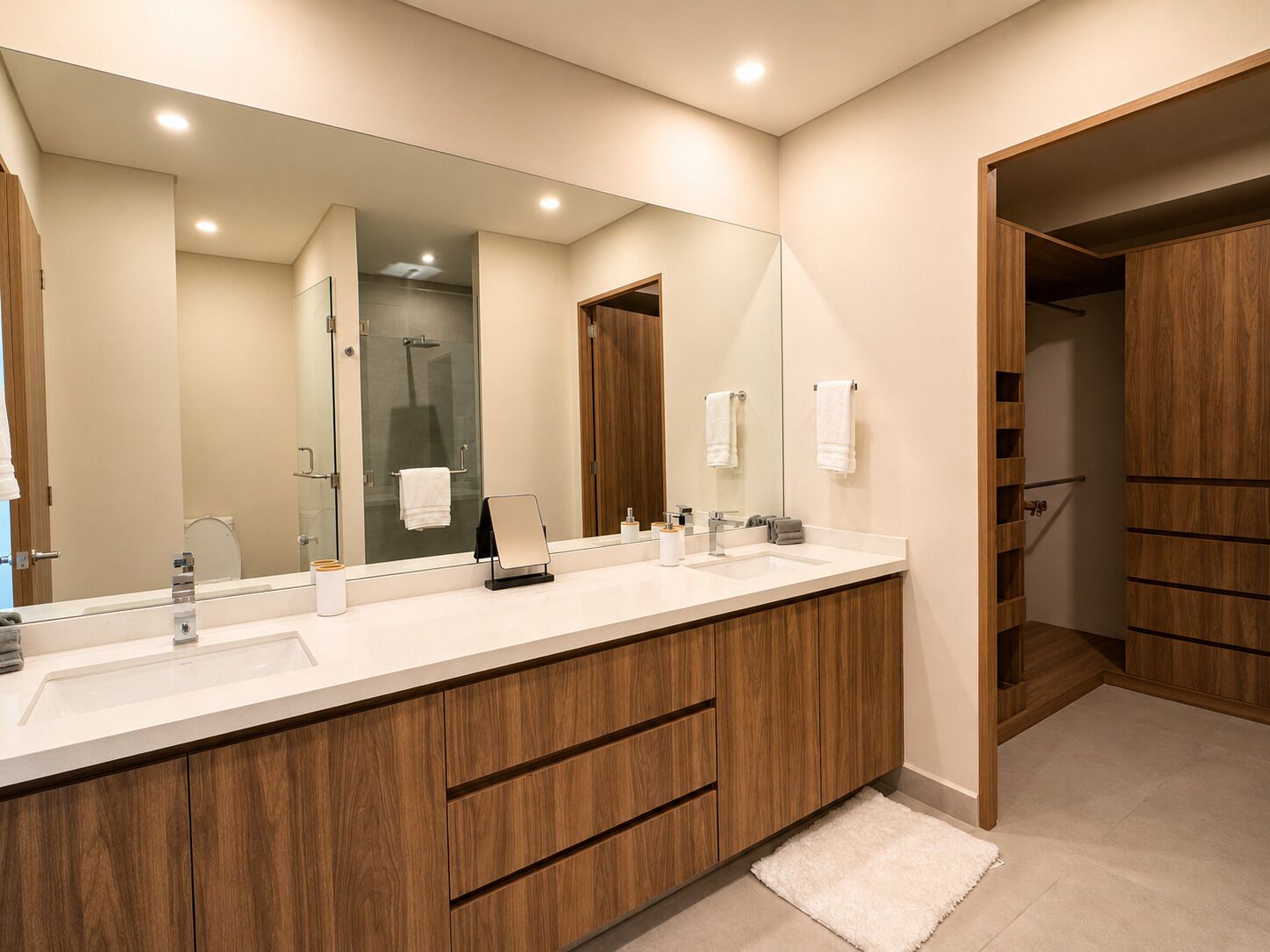 A modern bathroom with a large mirror, two sinks, wooden cabinets, and a shower area.