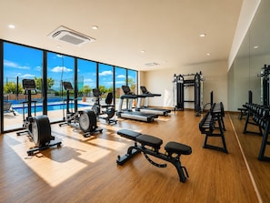 Et fitnesscenter med træningsmaskiner, vægtstationer og en swimmingpool, der ses gennem store vinduer.