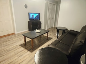 A living room with a black leather sofa, a coffee table, a television on a stand, and a small round table.