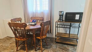 A dining area with a wooden table and chairs, a coffee maker, and a microwave on a shelf. - Bright & Cozy One Bedroom Getaway (Grand Falls-Windsor)