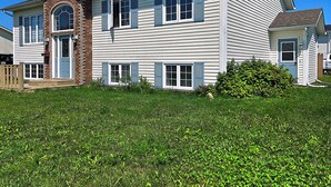 A two-story house with a front porch, a brick chimney, and a small attached garage. - Bright & Cozy One Bedroom Getaway (Grand Falls-Windsor)