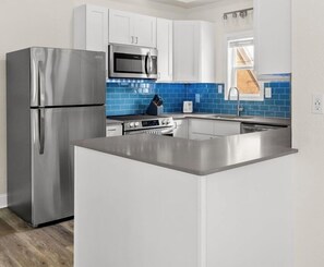 A modern kitchen with stainless steel appliances, white cabinetry, and a blue backsplash. - Walk to the Beach | 5 Minutes to St. Andrews State Park | Easy Access | Updated (Panama City)