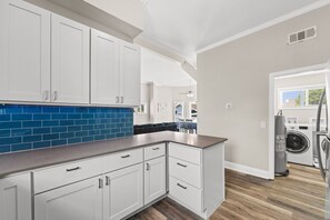 Une cuisine moderne avec des meubles blancs, un pare-feu bleu et un four encastré.