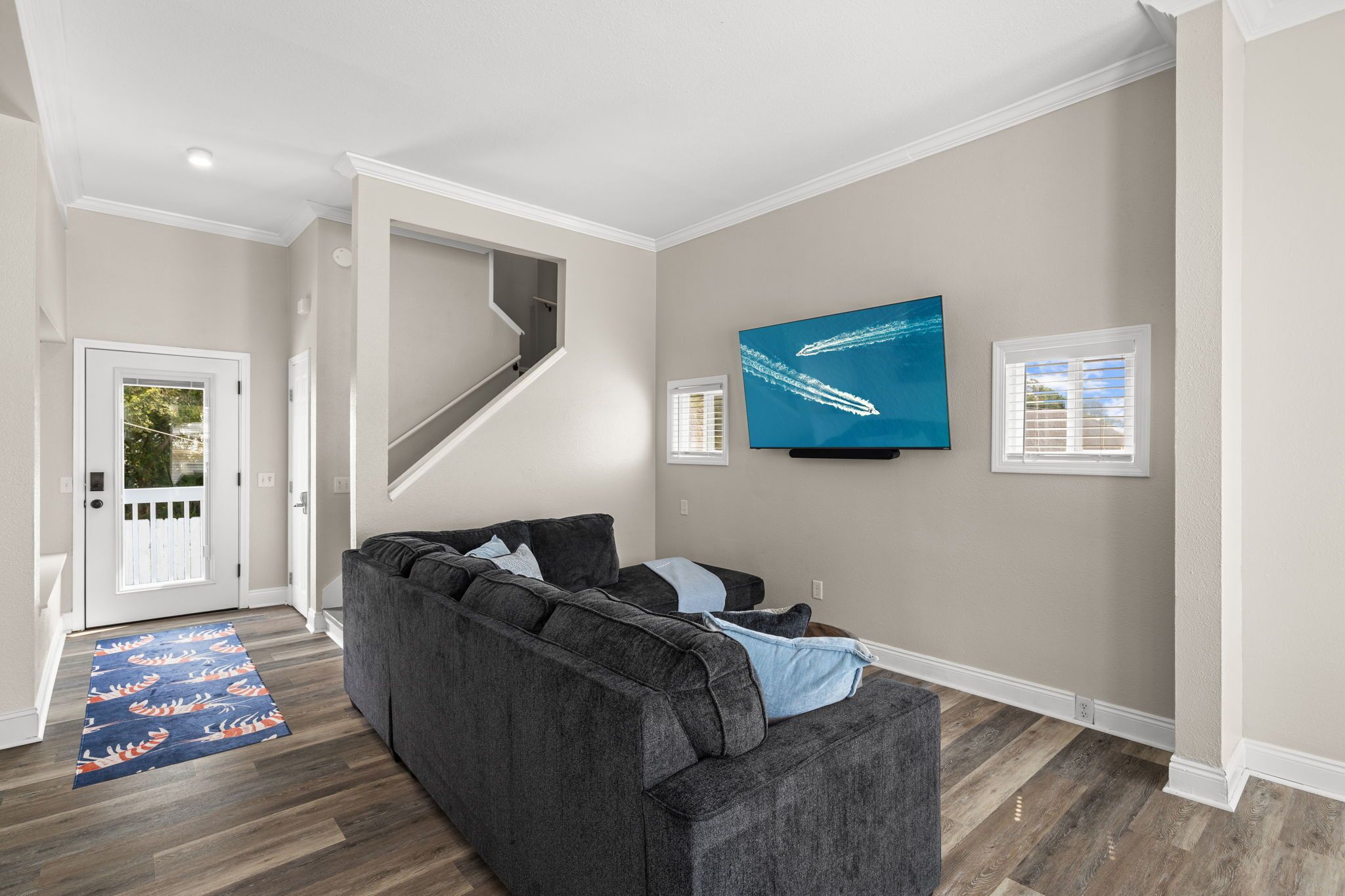 Un salon avec un canapé gris, un téléviseur à écran plat fixé au mur et un plancher en bois.