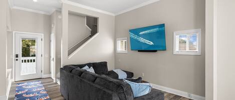 Ein Wohnzimmer mit grauem Sofa, einem flachbildfernseher an der Wand und Holzboden.