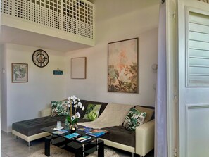 A living room with a sofa, coffee table, and wall art. - Lovely & Cozy 1-Bedroom Loft with AC & Tropical Patio, 5 Minutes from Marigot (Marigot)