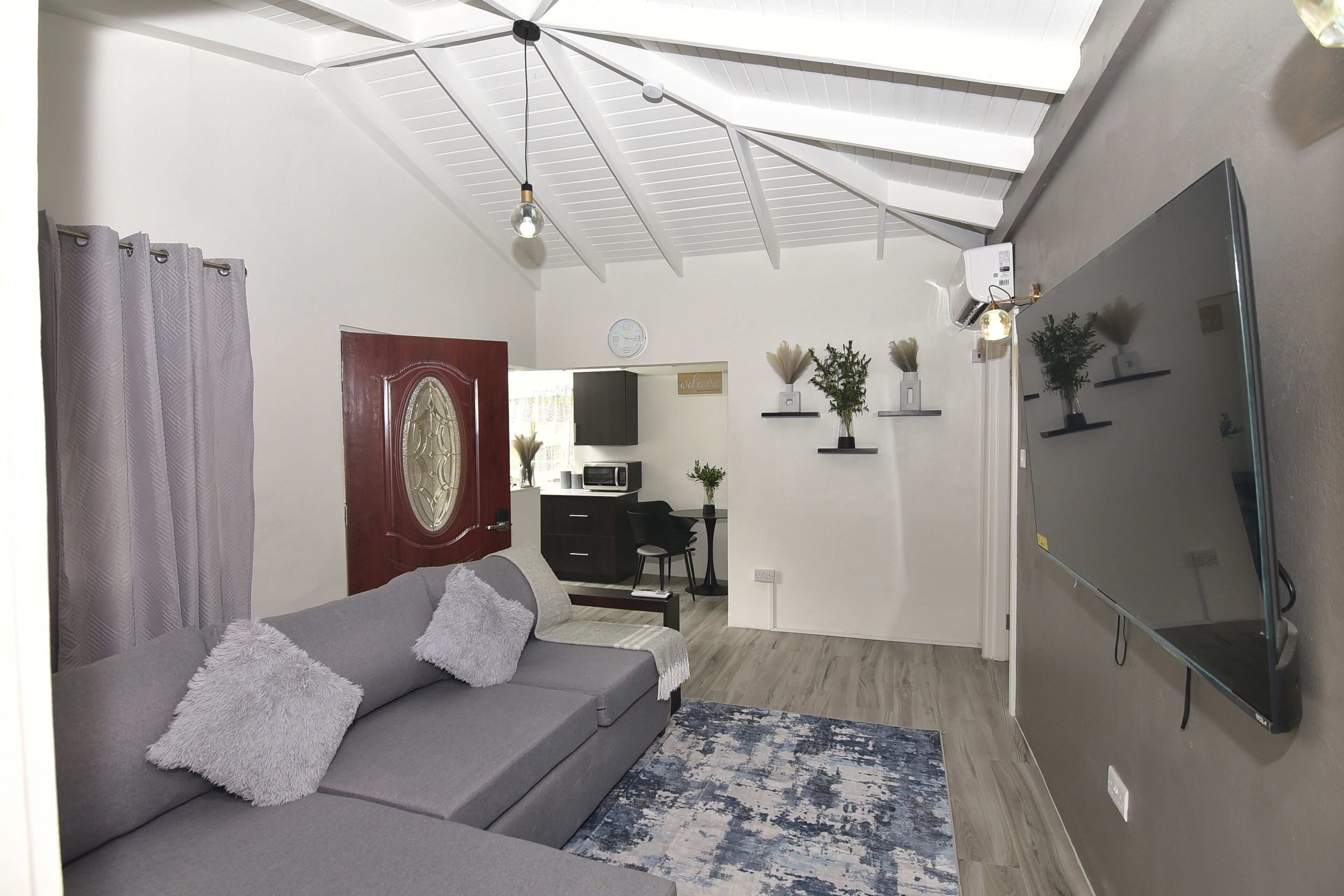 Een moderne woonkamer met een grijze bank, een tapijtend met patroon, een plafondventilator en een flatscreen-televisie aan de muur.