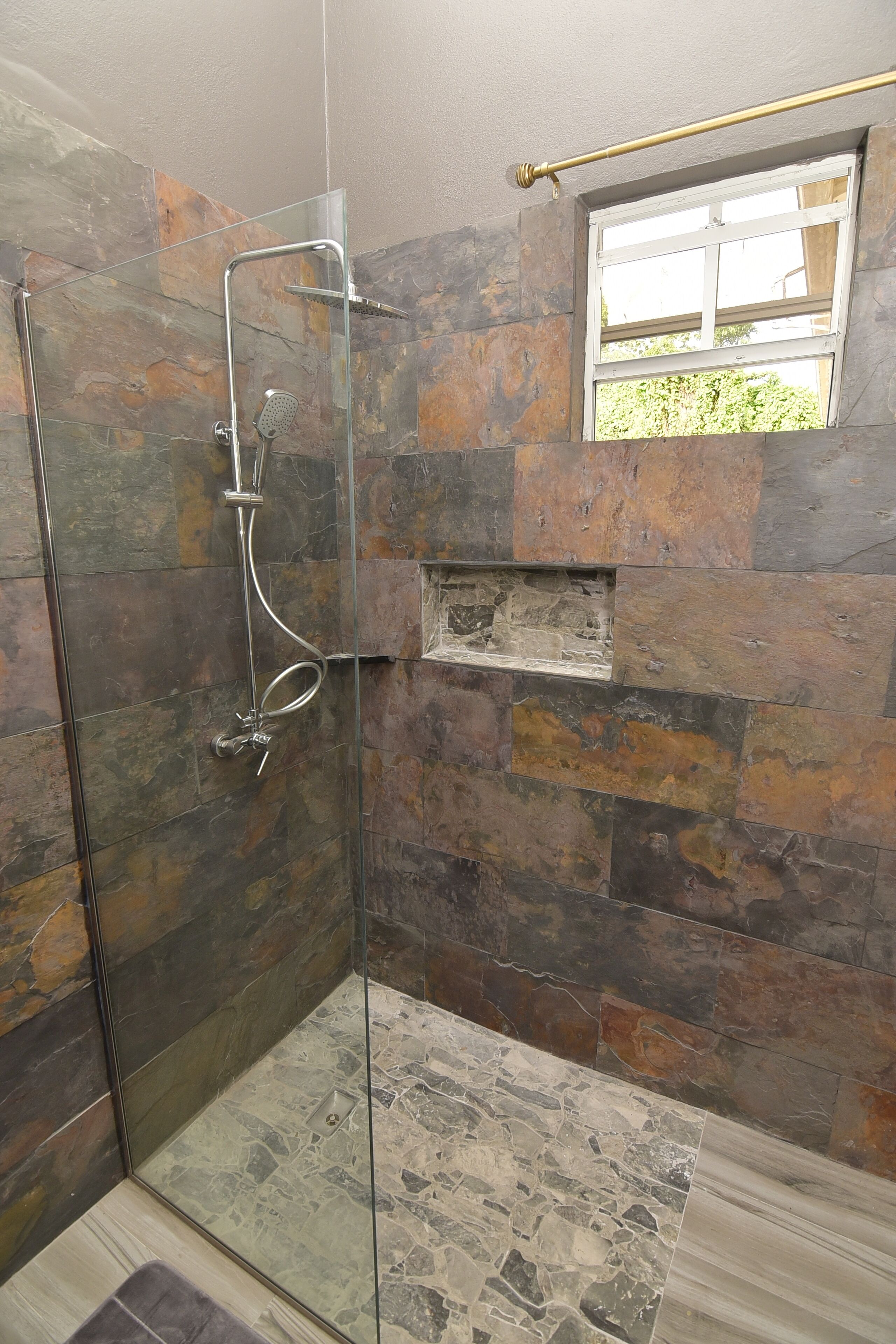 Een douche met een glazen deur en een stenen wand.