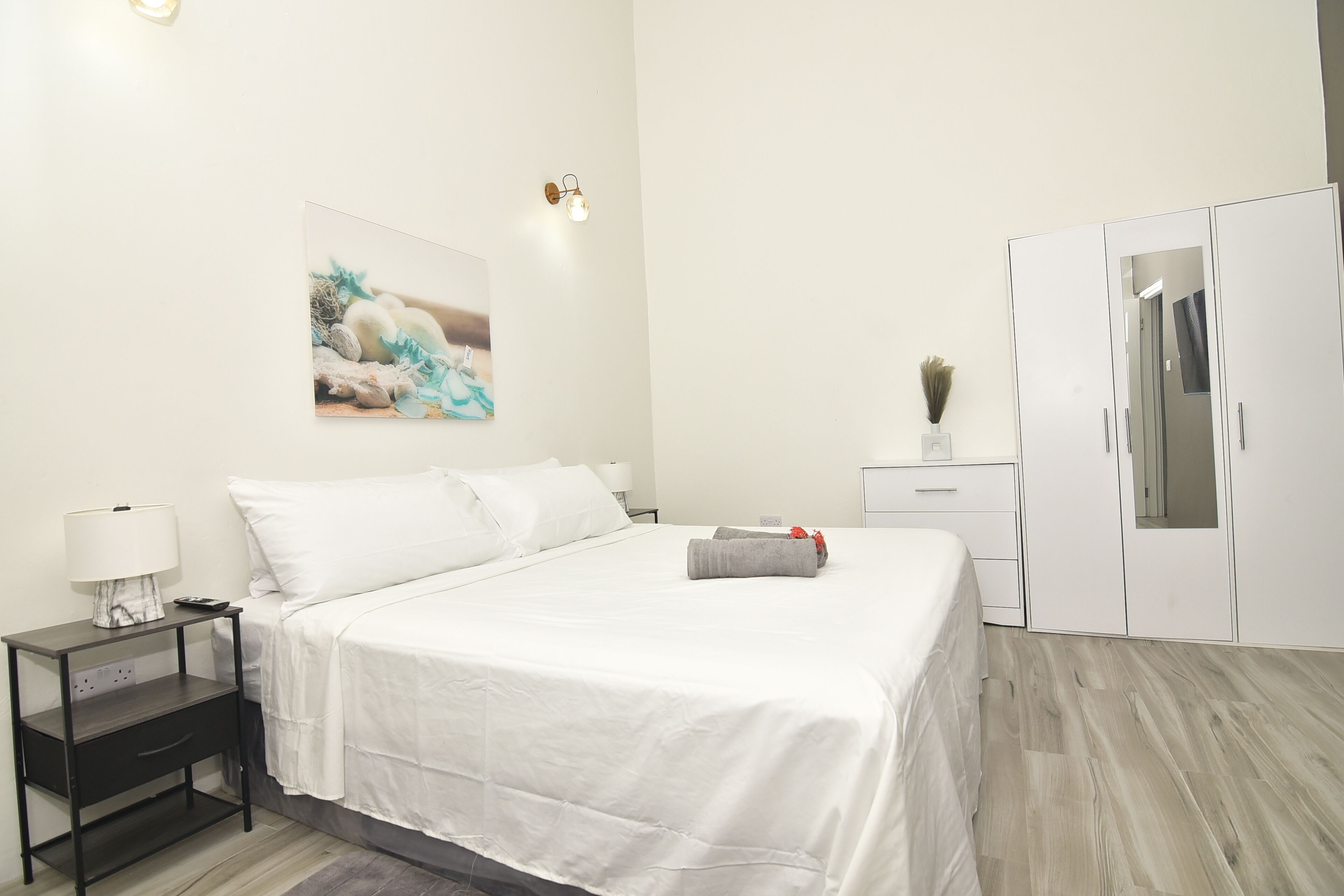 Een hotelkamer met een bed, nachtkastje, lamp, schilderij, kledingkast en spiegel.