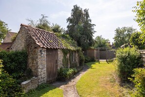 A stone cottage with a tiled roof, a wooden door, and a small garden with a paved path.