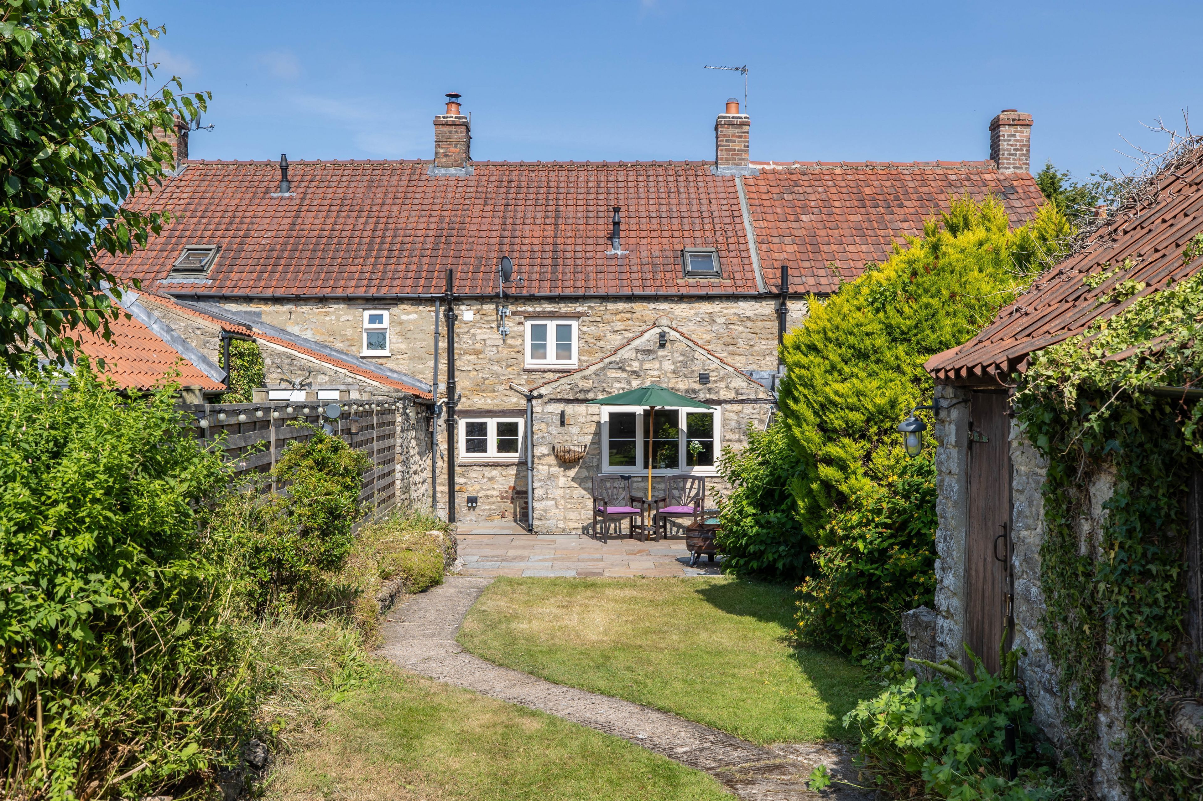 A stone house with a tiled roof, a paved driveway, and a small garden area.
