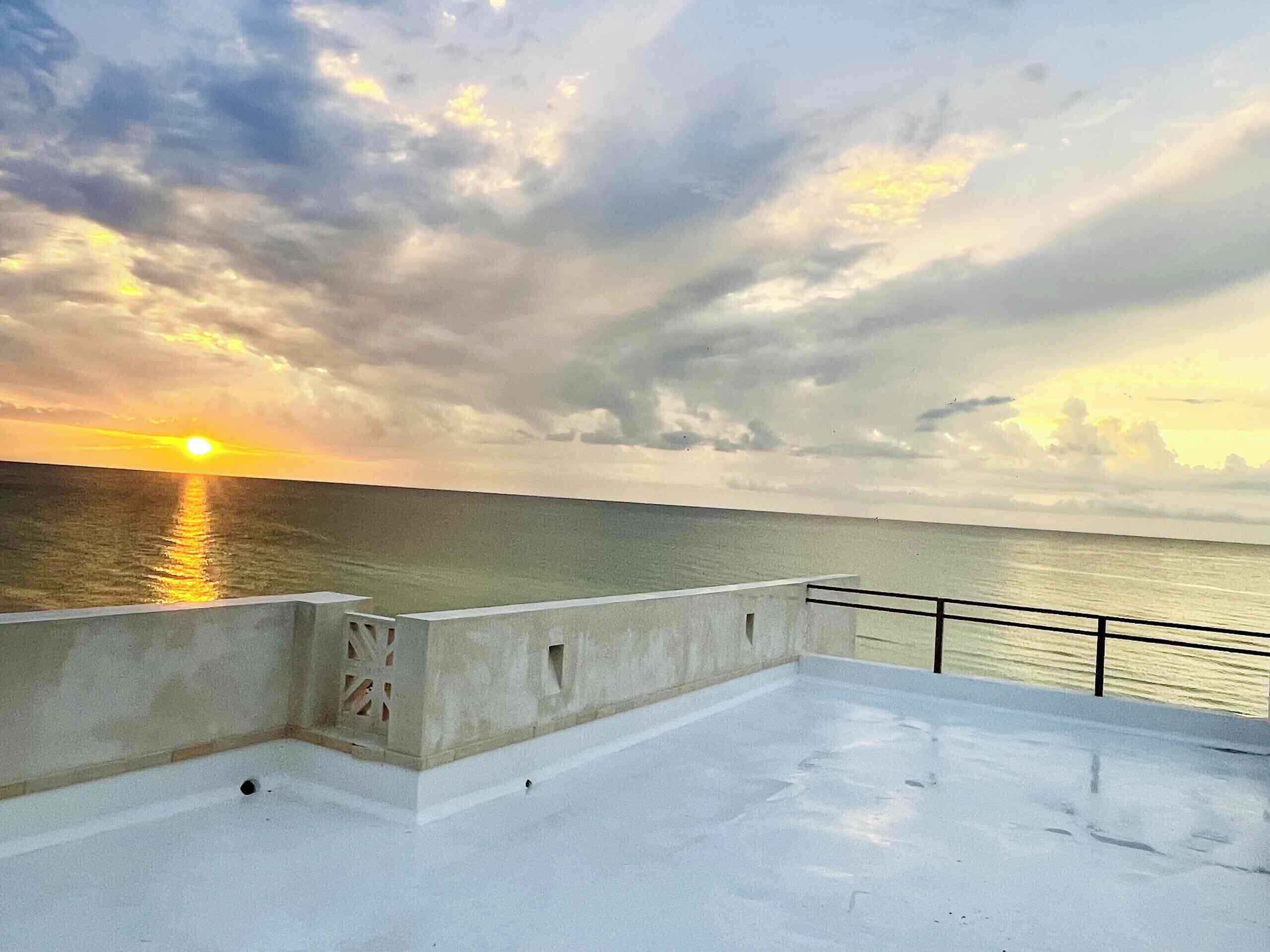 A rooftop terrace with a view of the sunset over the ocean.