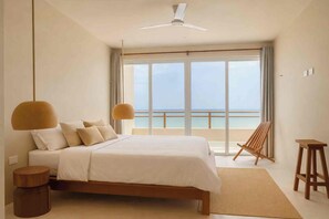 Ein Schlafzimmer mit Bett, Deckenventilator, Meerblick und einem Holzstuhl.
