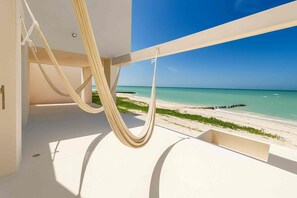 A hammock suspended from a balcony overlooking a beach with clear skies.