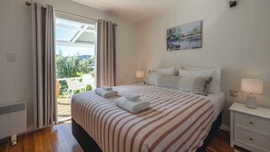 Una habitación de hotel con cama, dos mesitas de noche, un cuadro y vistas al verdor a través de la ventana.