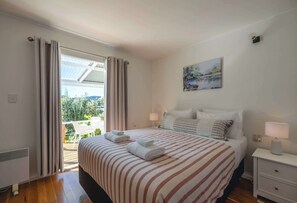 Ein Hotelzimmer mit einem Bett, zwei Nachttischen, einem Gemälde und Blick auf Grün durch das Fenster.