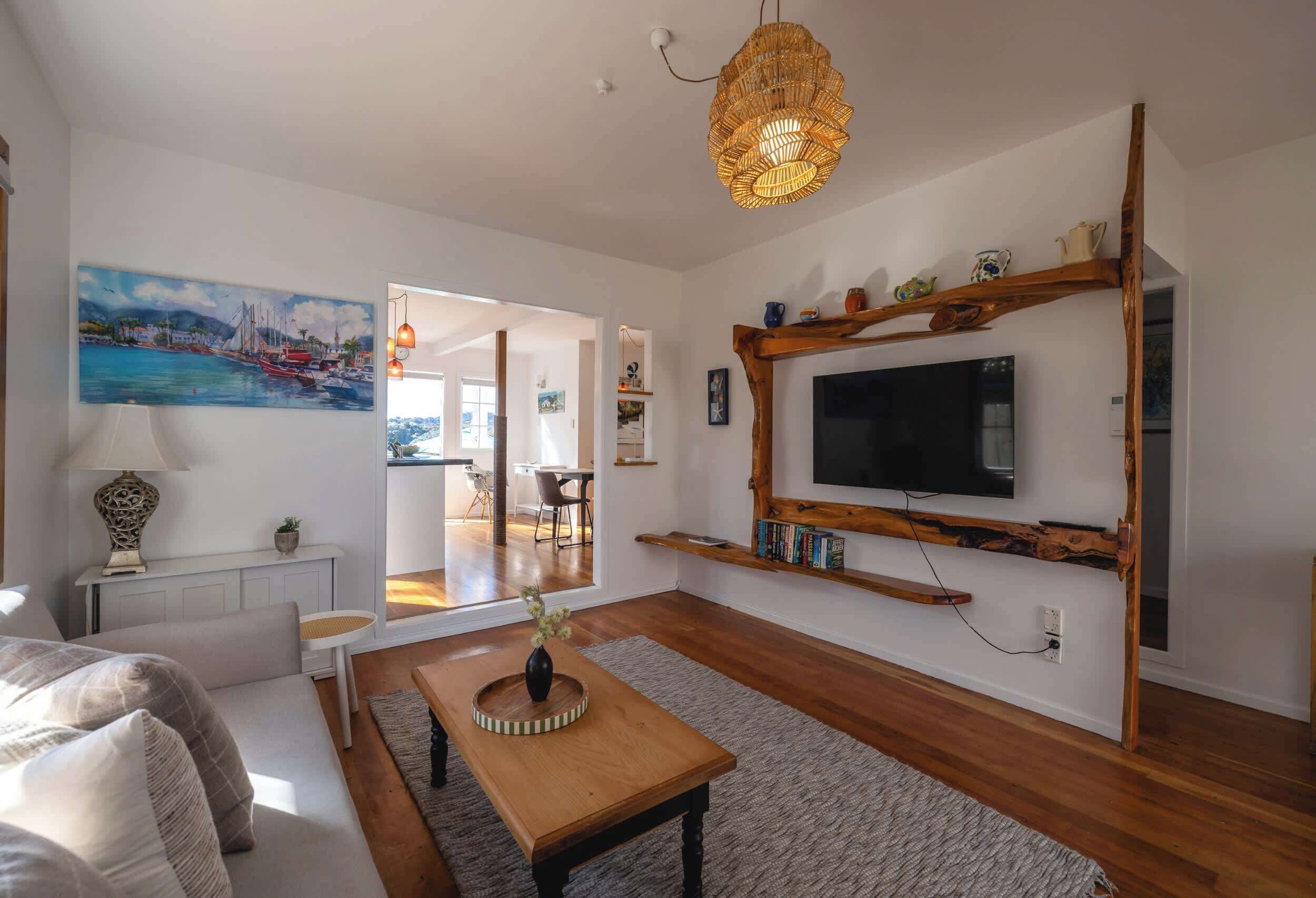 A modern living room with a flat-screen TV, wooden shelves, a dining area, and a painting on the wall.