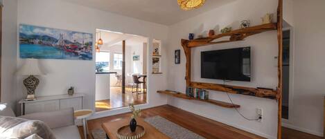 Un soggiorno moderno con televisione a schermo piatto, scaffali in legno, zona pranzo e un quadro appeso al muro.