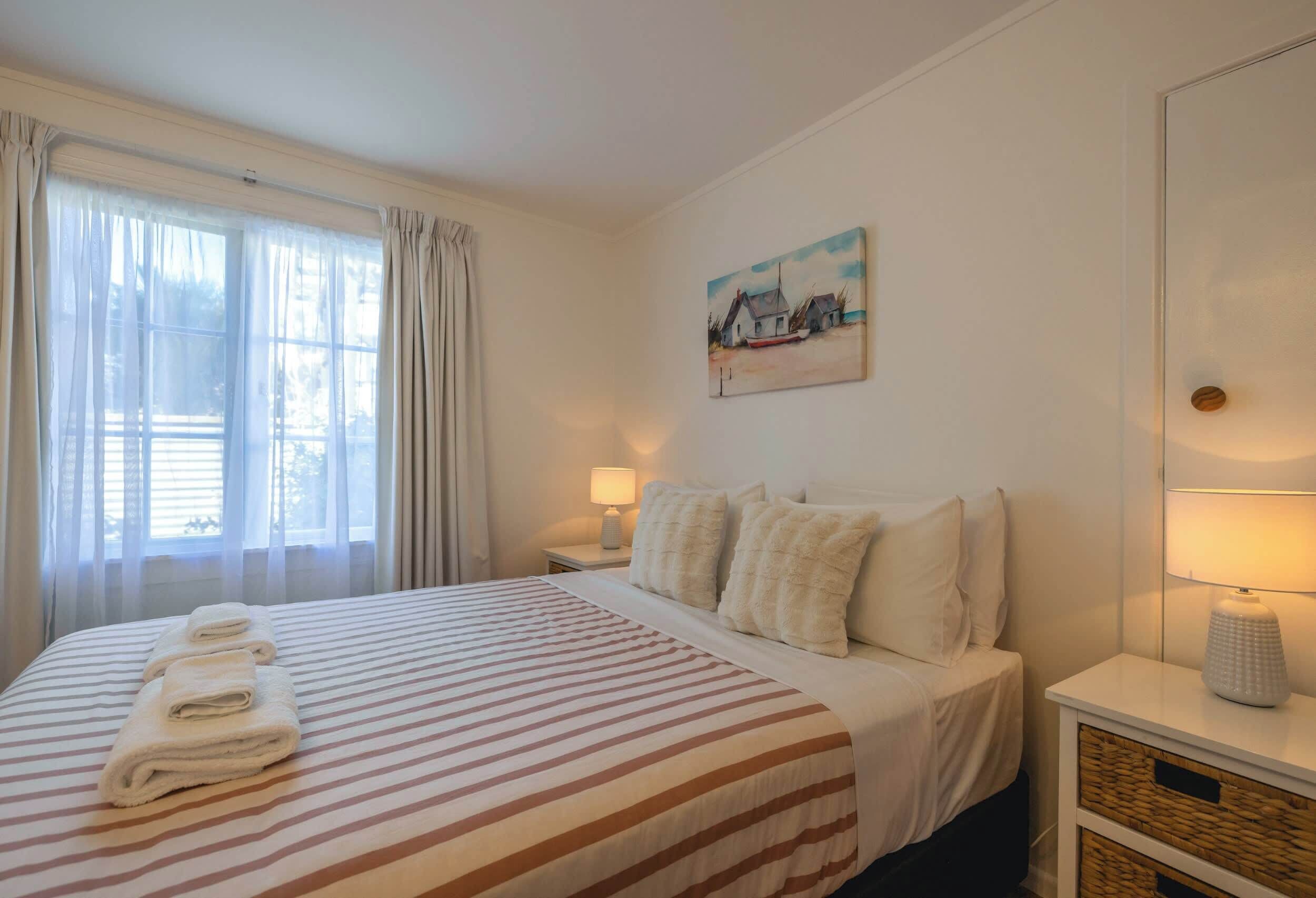 A hotel room with a bed, a painting, a nightstand, and a lamp.