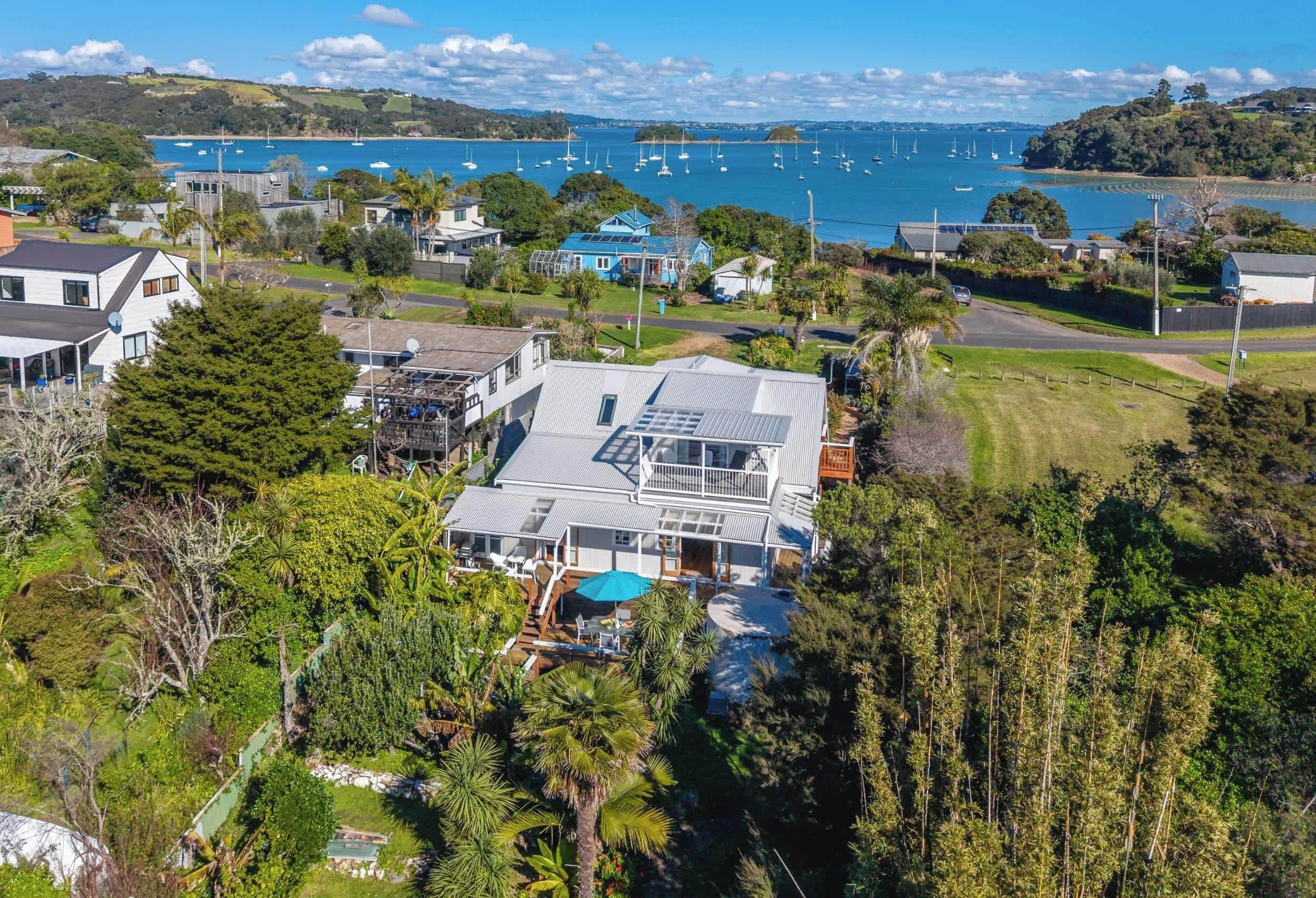 A large house with a spacious deck and a swimming pool, surrounded by lush greenery and a view of a bay with boats.