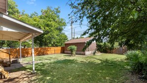 A backyard with a covered patio, a brick shed, and a wooden fence. - The Lucile - Spacious 4BR Extended-Stay Home | Fast Wi-Fi & Parking (Wichita Falls)